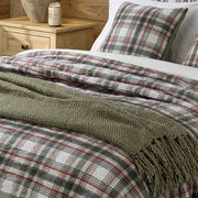 Close-up of the Woody quilt showing green and red plaid on a light background, with a green fringed throw and matching pillow.